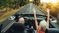 Rear view of an older couple driving down a country road in a convertible. 