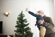 A grandparent holds up his grandkid so the kid can put the topper on top of the Christmas tree.