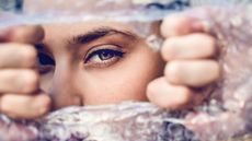 A woman tears a hole through bubble wrap as if it's blocking her view.