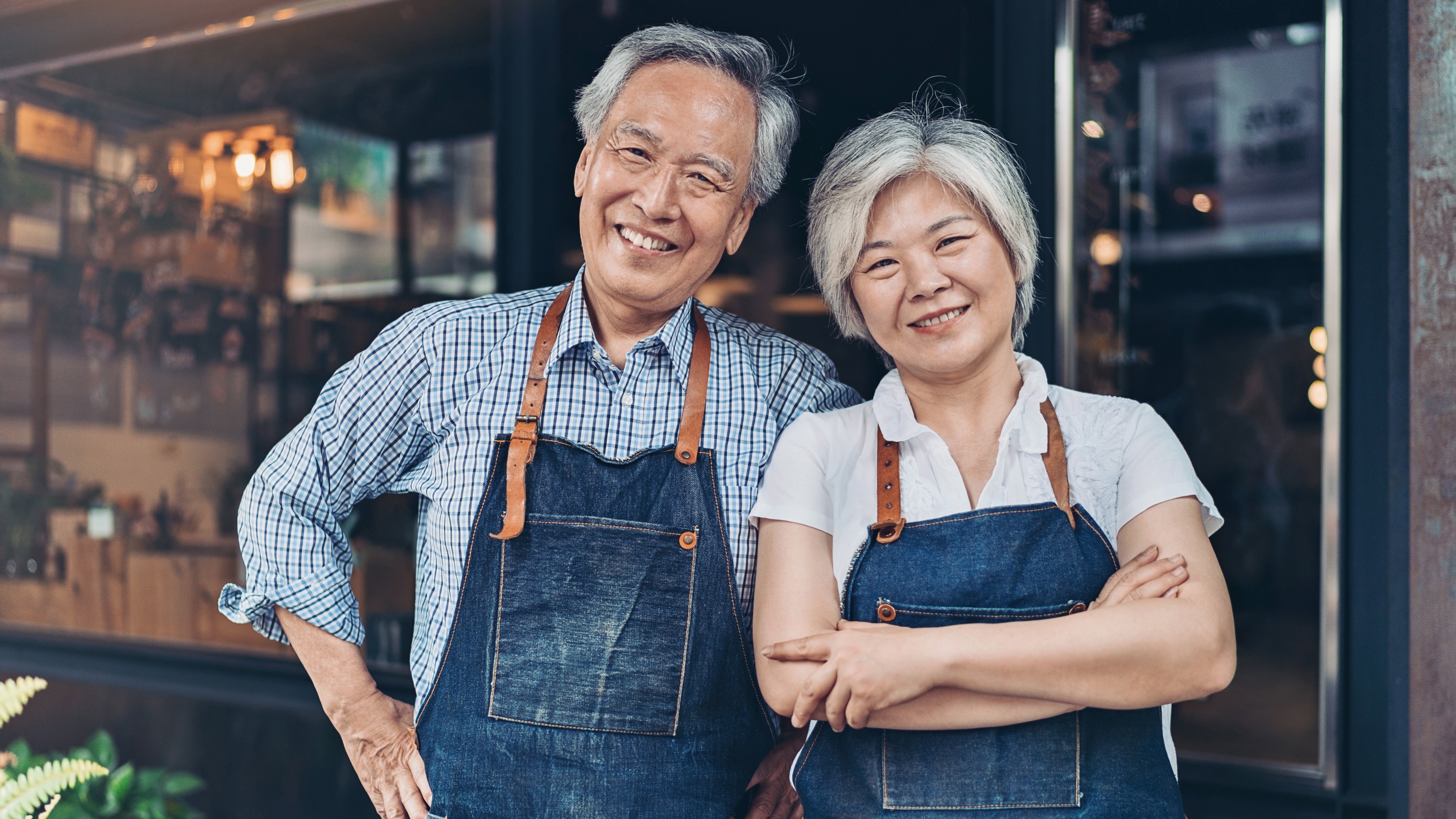 A couple of small business owners in aprons standing in front of their business.