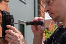 A man installs a video doorbell beside his front door.