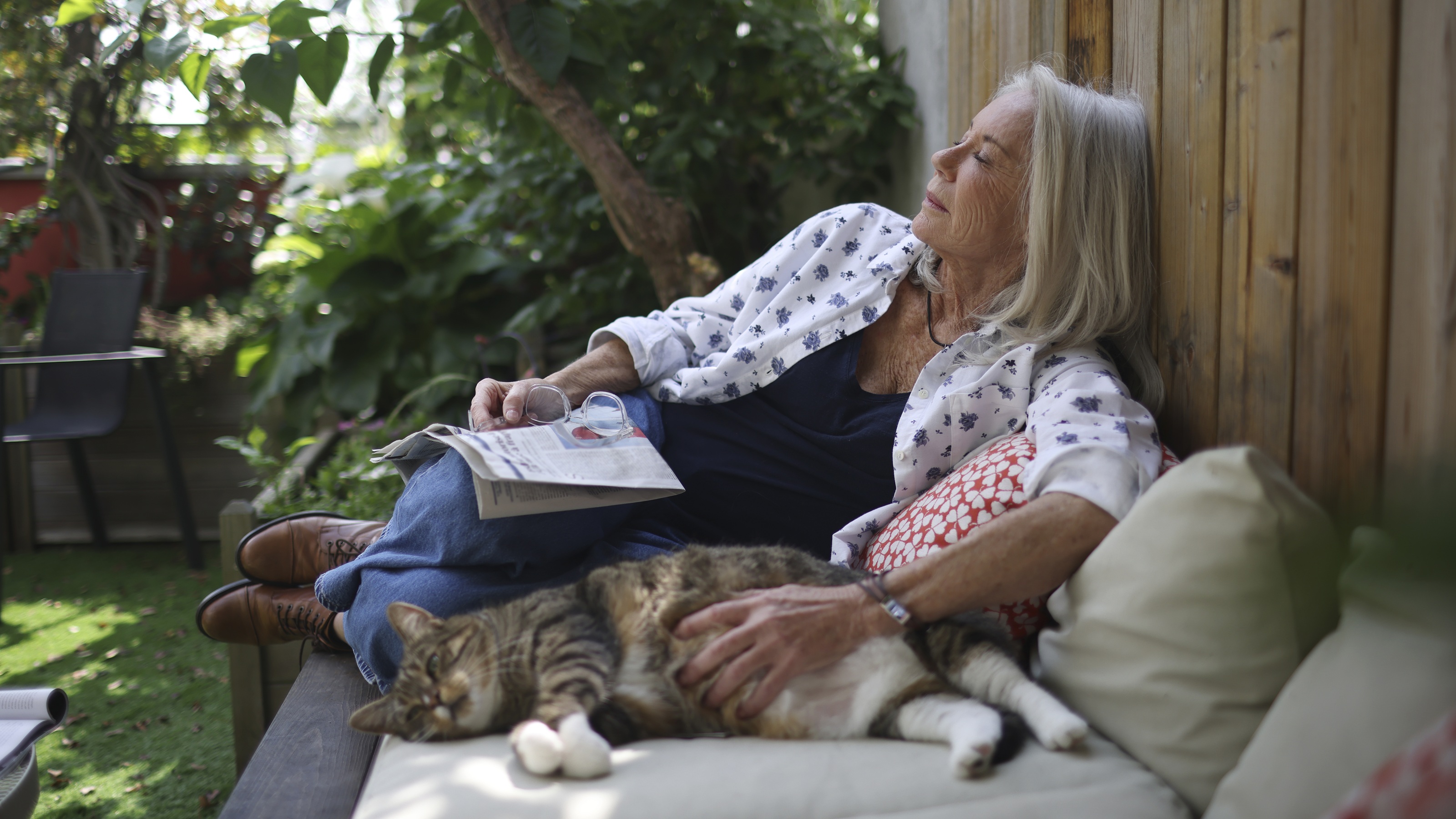 An older woman naps on her deck with her cat and a book.