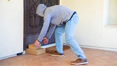 A man wearing a hoodie reaches for a package on a porch that isn't his.
