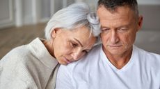 An older couple looking stressed console each other.