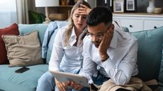 A couple appear frustrated as they look at a table together on their sofa.