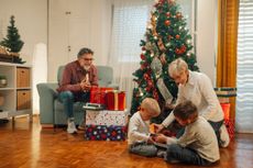 Grandparents sitting with kids by a Christmas tree while opening Christmas gifts.