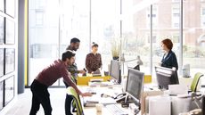 Four employees have a discussion around their desks.